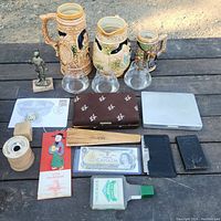 Photo showing stein mugs, whiskey glasses, ceramic pitcher, Canadian dollar bill, statuette, wooden fan and assorted items