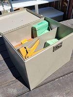 Closed metal box on outdoor surface, showing front and top view with latch lock.
