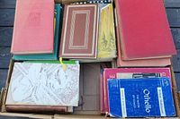 Top view of a box containing a variety of vintage hardcover and paperback books in assorted colors and conditions, showing wear and yellowing.