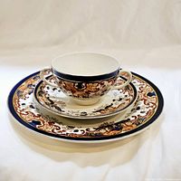 Photo showing the double-handled cup placed on saucer and salad plate, highlighting the ornate cobalt blue, gold, and brown Lucanina pattern design.