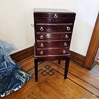 Front view of the vintage Bombay Company mahogany silverware chest on its matching legged base stand, showing five drawers with silver-tone ring pull handles and side metal handles on the chest.