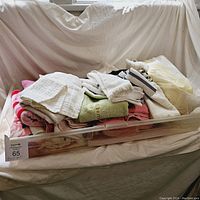 Overall view of the towel lot inside a plastic storage bin. Mixed colors and textures visible.