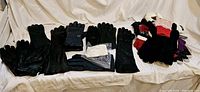 Wide view showing many pairs of black leather gloves, single black gloves, and a pile of colorful newer gloves