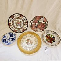 Photo showing five antique and vintage decorative plates with various floral and fruit motifs, some with gold trim.
