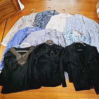 Overview of all tops arranged on floor showing mix of striped blouses, floral blouse, and black embellished tops