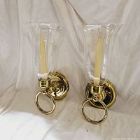 Front view of the pair of brass and glass wall sconces with taper candles inserted, showing polished finish and design details.