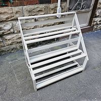 Front view of a vintage solid wood plant stand with four slatted shelves painted white, showing overall condition and structure.
