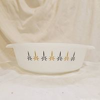 Side view showing the black and gold starburst pattern on white glass casserole dish with handles