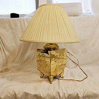 Full view of vintage brass urn lamp with pleated cream lamp shade on a white backdrop.
