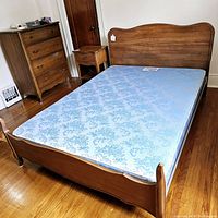 Full view of bed frame with box spring, nightstand and chest of drawers in a room with hardwood floor.
