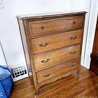 Front left side view of the tall dresser showing details of the wood finish, four drawers with metal handles, and tapered legs.