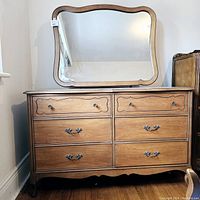 Front view of six-drawer wooden dresser with scalloped bottom apron and metal pulls, mirror attached