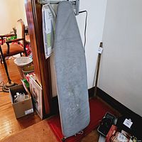 Full view of the gray ironing board with some wear on the fabric cover and a red base.