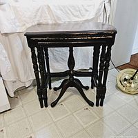 Three vintage mahogany nesting tables stacked showing front edge wear and spindle legs