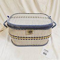 Closed view of the rectangular woven wicker sewing basket in white, natural, and blue colors with two handles and latch closure.
