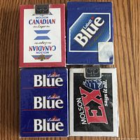 Four unopened decks of beer-themed playing cards arranged on wood surface, showcasing Molson Canadian, Labatt Blue, and Molson Ex branding.