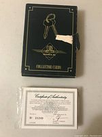 Black collector card box with gold graphics and visible damage on the side. Box shows unopened card package inside.