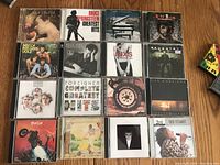 Top-down photo showing 15 rock and classic rock CDs arranged in a grid, covers visible including Heart, Bruce Springsteen, Bee Gees, Billy Joel, INXS, Pink Floyd, Meat Loaf, and others.