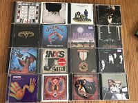 Top view of 16 rock music CDs arranged in a 4x4 grid showing album covers including Foreigner, Foo Fighters, Adele, Van Halen, Steve Miller Band, The Killers, Def Leppard, INXS, Wingspan, and others.