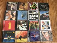 Photo of 15 rock music CDs laid out on a wooden surface, showing cover art and titles.