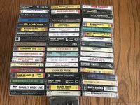 Photo showing assortment of country music cassette tapes arranged on a surface, featuring titles and artists' names on the spines.