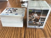 Stack of hockey cards including Teemu Selanne card on top and a protective plastic case containing Alexandre Daigle card