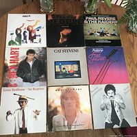 Top down view of nine LP vinyl records arranged in a 3x3 grid on a wooden table, showing cover artwork. Covers have minor surface wear.