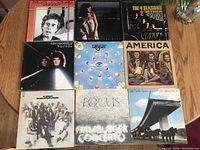 Full view of 9 LP vinyl records arranged in 3x3 grid on wooden surface. Visible album covers with band and artist names.