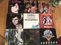 Photo showing 9 LP vinyl record album covers laid out in a 3x3 grid on a wooden floor.