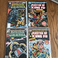 Four vintage comic books laid flat on wood surface showing two Battlestar Galactica and two Master of Kung Fu issues.