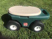 Side view of the garden hopper showing the green plastic body, black wheels, and beige seating surface.