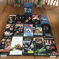 Lot of 17 VHS tapes arranged on a wooden table showing covers of various movies and one Aerosmith music tape