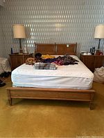 Front view of full-size wood bed frame with mattress and surrounding nightstands and lamps