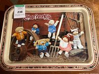 Front side view of the metal tray with Cabbage Patch Kids dolls image and a sticker on corner.