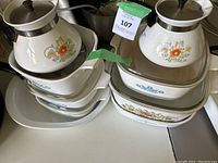 Overview photo showing mixed CorningWare pots, casserole dishes and baking dishes stacked and arranged, featuring various vintage floral patterns.
