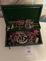 Opened green velvet-lined jewelry box showing top tray with mixed items