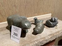 Four soapstone animal carvings displayed on a stone surface against a wall, including a bear and three bird figures.