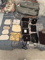Wide view of 14 vintage ladies purses and matching pair of black embroidered gloves on bed showing colors, types, and arrangement