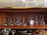 Shelf displaying twelve vintage crystal cordial glasses upside down, showing bowls and bases, with air twist stems visible.