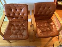Two mid-century modern style armchairs with brown tufted leather cushions and wooden frames shown from top view on wooden floor.