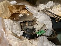 Partially visible ornate silver-tone platters wrapped in tissue paper and plastic, showing etched floral patterns and scalloped edges