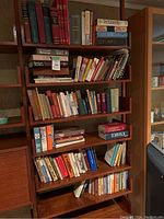 Image showing a fully stocked wooden bookshelf with multiple shelves featuring mixed books of various genres and formats. Highlights the overall quantity and condition.