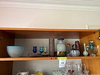 Wide view of upper wooden shelf showing multiple mixed mid-century modern decorative items including glass, ceramics, and metal items.