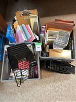 Overview of two plastic crates containing assorted office supplies including clipboards, file folders, binders, staplers, and organizational trays.