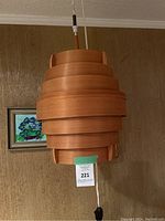 Front view of hanging wood slat pendant lamp suspended from ceiling with cord and pull switch visible