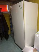 Side angle view of the upright freezer showing it standing in a room with nearby items.