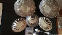 Five bowls (two ornate repousse, one plain round, two scalloped ovals) and two spoons arranged on table