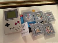 Original Game Boy console with six cartridges in clear protective cases alongside printed auction lot tag