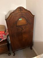 Photo showing the closed front of the vintage walnut wardrobe with carved wooden detailing and curved top design.