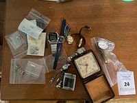 Photo of various wristwatches, watch parts and a vintage square desk clock in a leather display box on wooden surface